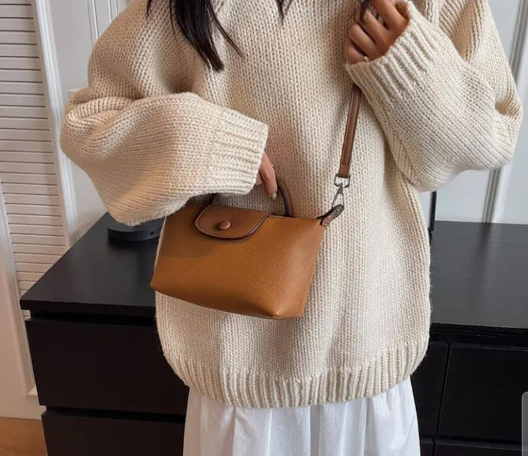 NCHIMBA tan pebble-textured vegan leather mini top-handle crossbody bag with a flap closure worn with a knit sweater.